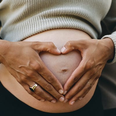 Ventre rond, mains des parents en cœur sur un pull beige