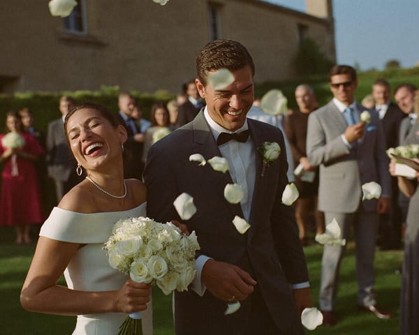 Les mariés rient sous une pluie de pétales blancs, entourés de leurs invités