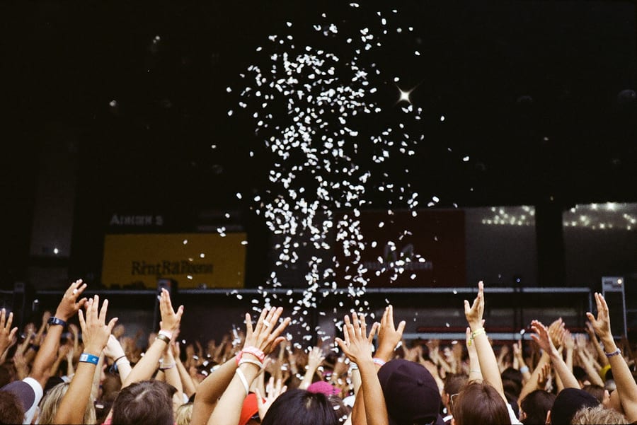 Confettis au-dessus d'une foule bras levés, scène en fond